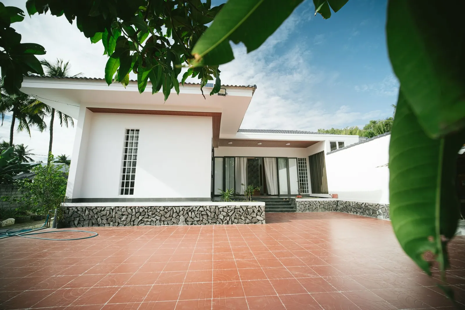 White house with deep eaves and a terracotta-tiled terrace framed by banana leaves