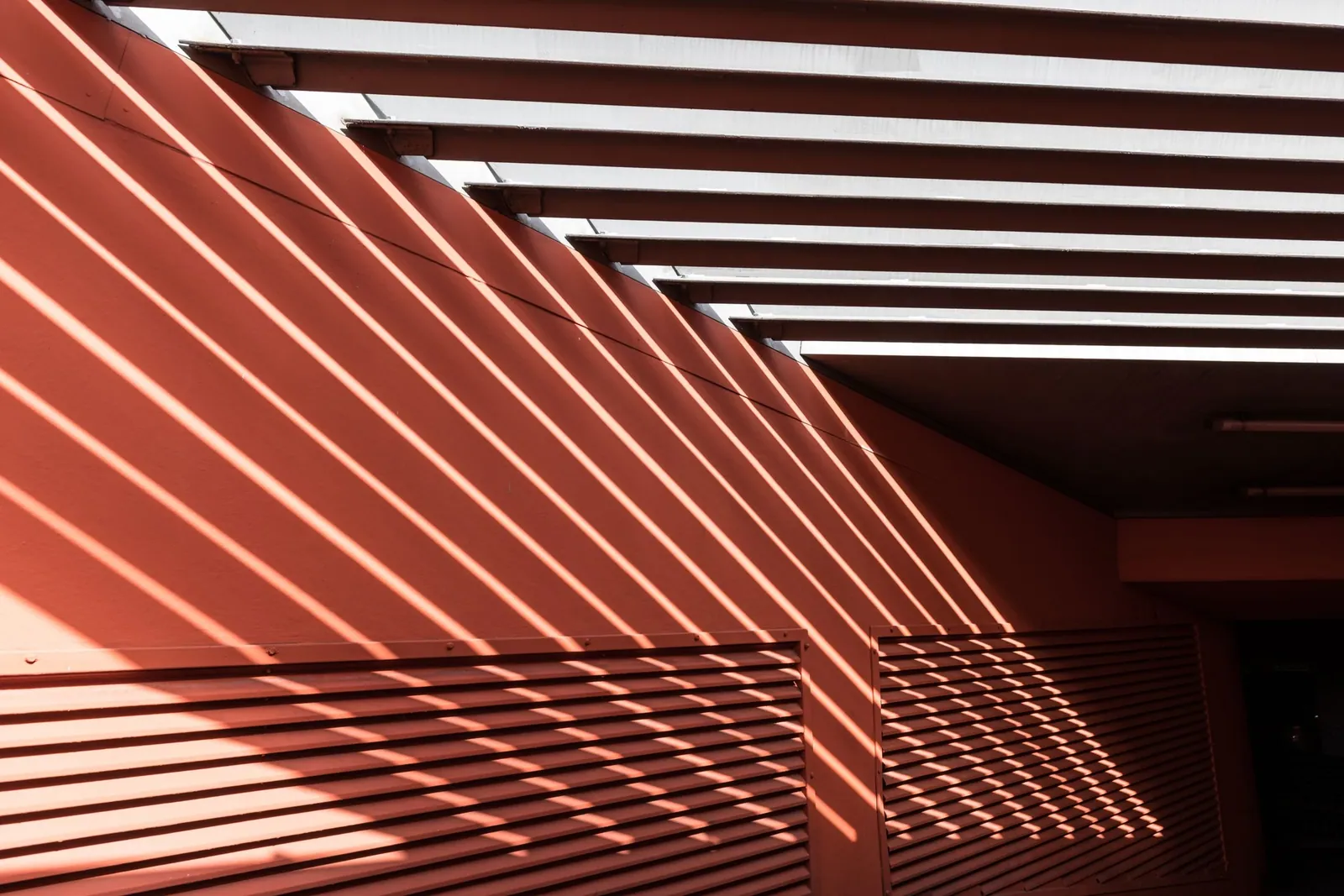 Sunlight casting striped shadows through a pergola onto a terracotta wall